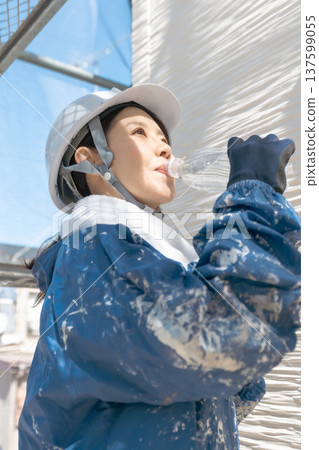 Preventing heatstroke on summer construction sites: A female worker hydrates and wipes away sweat between tasks 137599055