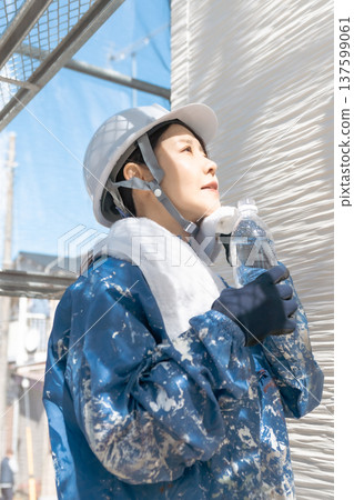 Safety and health management in the construction industry: A woman wearing a helmet refreshing herself between work tasks Safety and health management in the construction industry: A woman wearing a helmet refreshing herself between work tasks 137599061