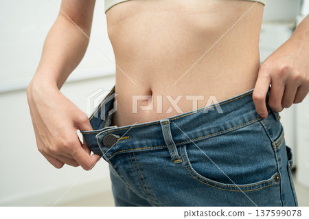 Young Asian woman losing weight wearing loose pants in oversize jeans. 137599078