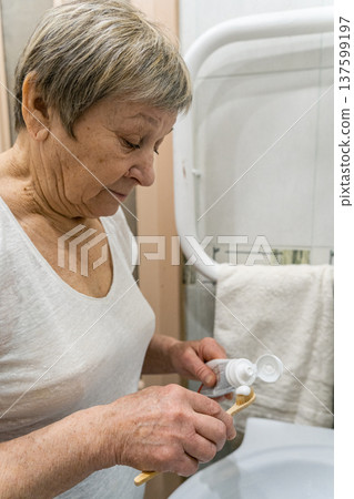 Senior woman applying toothpaste to bamboo toothbrush in her bathroom, preparing for morning oral hygiene routine, focusing on daily dental health, personal care. Real life of an elderly person Senior woman applying toothpaste to bamboo toothbrush in her bathroom, preparing for morning oral hygiene routine, focusing on daily dental health, personal care. Real life of an elderly person 137599197