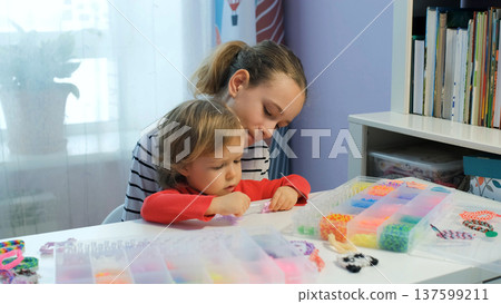 A teen girl helps her little sister create colorful rubber band bracelets while enjoying time together 137599211