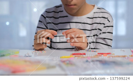 A teenage girl works on a beaded bracelet at her desk threading beads and organizing colorful supplies with care and creativity 137599224