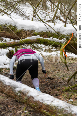A female athlete ducks under fallen, snow-covered trees A female athlete ducks under fallen, snow-covered trees 137599285