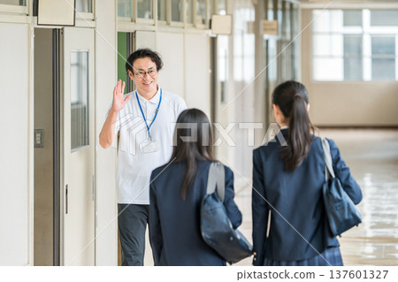 A male teacher and female students greeting each other in a school hallway 137601327