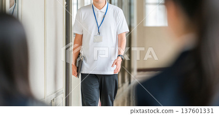 A male teacher in a polo shirt walking down a school corridor 137601331