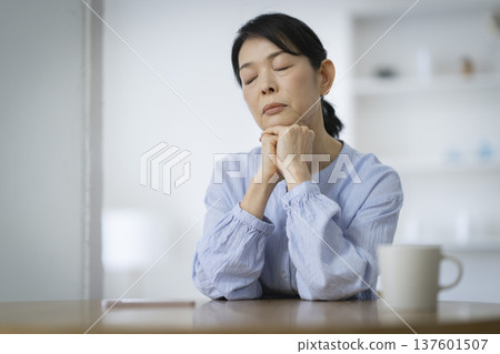 A woman in her late 50s lost in thought with her chin resting on her hands 137601507