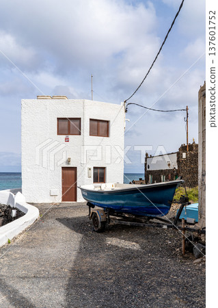 A quaint boat rests on a trailer beside a white building in Punta Mujeres, Lanzarote. The architecture blends with the coastal scenery. 137601752