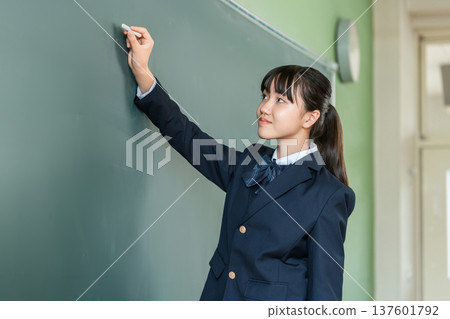 A female junior high school student writing with chalk on a blackboard in the classroom 137601792