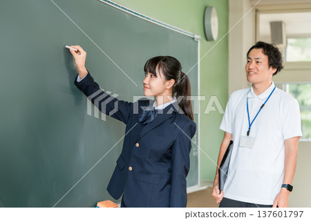 一名國中女生和一名男老師在課堂上用粉筆在教室黑板上寫字 137601797