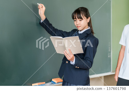 一名國中女生和一名男老師在課堂上用粉筆在教室黑板上寫字 137601798