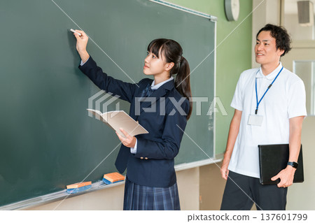一名國中女生和一名男老師在課堂上用粉筆在教室黑板上寫字 一名國中女生和一名男老師在課堂上用粉筆在教室黑板上寫字 137601799
