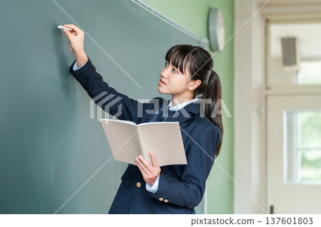 A female junior high school student writing with chalk on a blackboard in the classroom 137601803