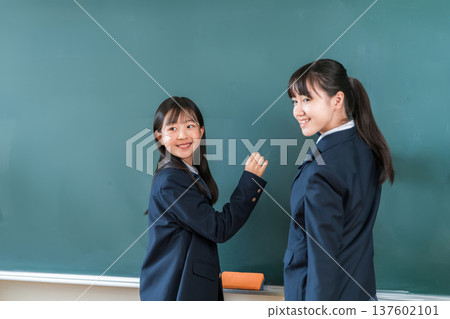 一名國中女生在教室的黑板上用粉筆寫字 一名國中女生在教室的黑板上用粉筆寫字 137602101