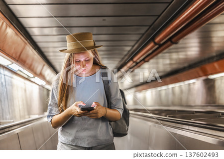 Young woman using smartphone while riding escalator in subway tunnel, urban commuting lifestyle 137602493