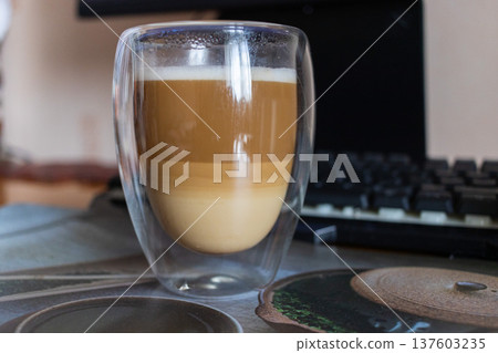 Layered Latte Macchiato in Double Walled Glass on Desk with Mechanical Keyboard Layered Latte Macchiato in Double Walled Glass on Desk with Mechanical Keyboard 137603235