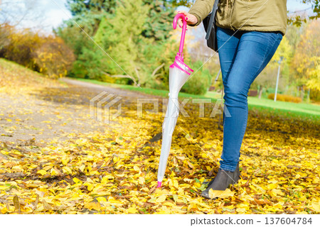 Woman walking in park with umbrella Woman walking in park with umbrella 137604784