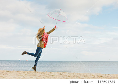 Woman jumping with transparent umbrella on beach 137604785