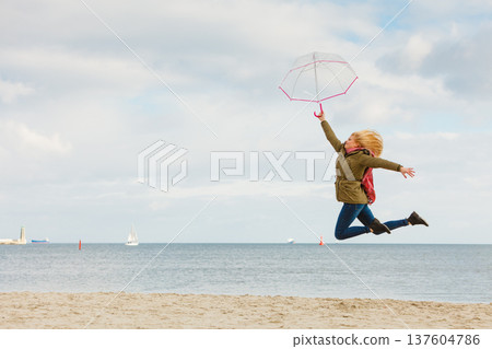 Woman jumping with transparent umbrella on beach 137604786