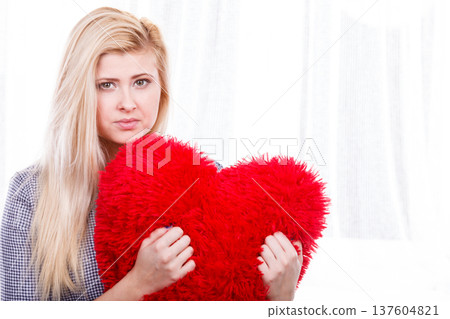 Sad woman holding red pillow in heart shape Sad woman holding red pillow in heart shape 137604821