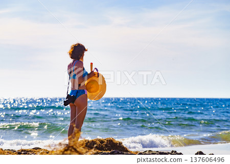 Woman in bikini with camera walk on beach Woman in bikini with camera walk on beach 137606496