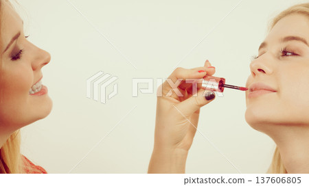 Woman applying her friend lipstick on lips Woman applying her friend lipstick on lips 137606805