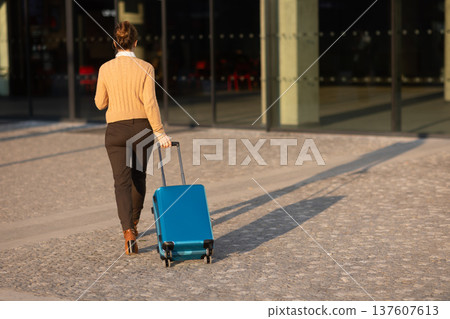 Woman Pulling Carry-on Suitcase Through Modern Transit Hub Woman Pulling Carry-on Suitcase Through Modern Transit Hub 137607613