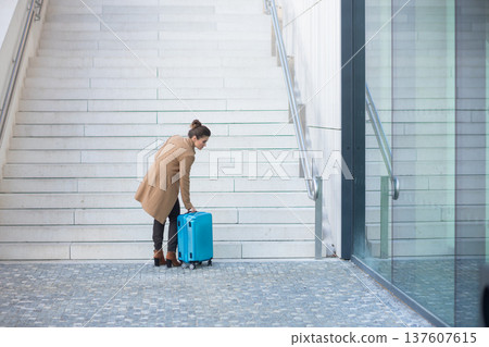 Woman Adjusting Suitcase at Train Station Stairs 137607615