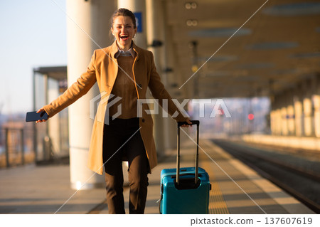 Happy Woman Arriving at Train Station with Suitcase 137607619