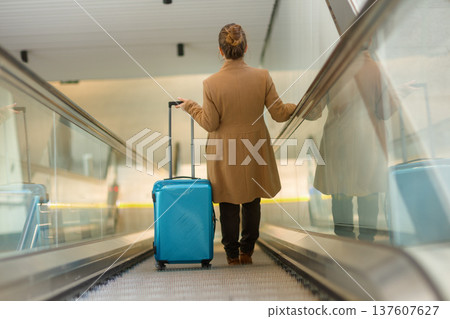 Woman with Blue Suitcase Ascending Station Escalator 137607627