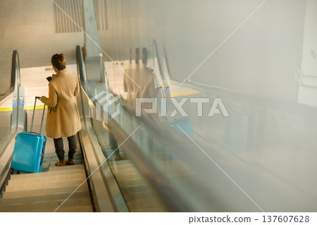 Woman Using Smartphone on Escalator with Suitcase 137607628