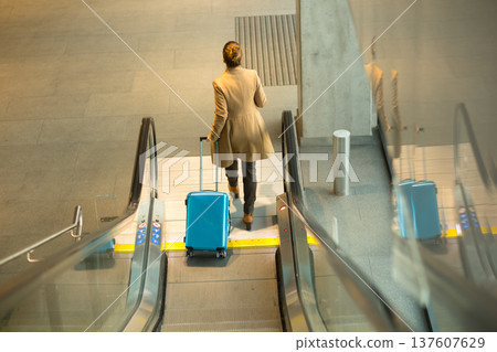 Woman with Blue Suitcase Ascending Modern Escalator 137607629
