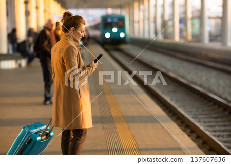 Woman Waiting on Train Platform with Smartphone 137607636