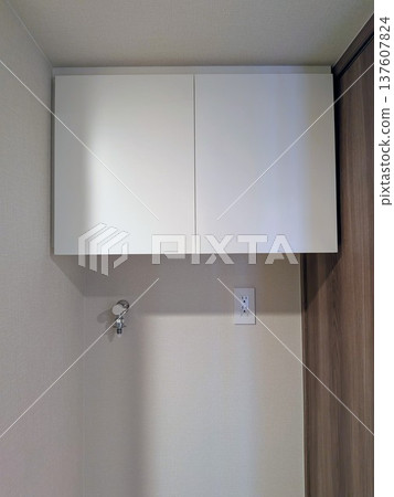 A white laundry cabinet with a faucet and outlet installed in the washing machine area of an apartment building 137607824