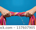 Close up of hands wringing water out of a wet striped beach towel with a splash and dripping liquid 137607905
