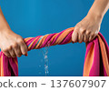 Close up of hands wringing water out of a wet striped beach towel with a splash and dripping liquid 137607907