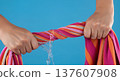 Close up of hands wringing water out of a wet striped beach towel with a splash and dripping liquid 137607908