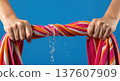 Close up of hands wringing water out of a wet striped beach towel with a splash and dripping liquid 137607909