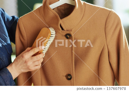 Close-up of Hand Brushing a Tan Wool Coat for Maintenance 137607978