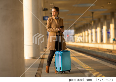 Woman with Suitcase Checking Phone at Train Station Woman with Suitcase Checking Phone at Train Station 137608025