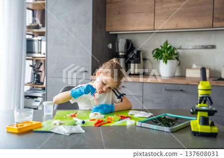 Young girl stirring chemical solution with measuring spoon in cup during crystal growing experiment at home. Chemistry practice and early STEM education through practical laboratory activity. Young girl stirring chemical solution with measuring spoon in cup during crystal growing experiment at home. Chemistry practice and early STEM education through practical laboratory activity. 137608031