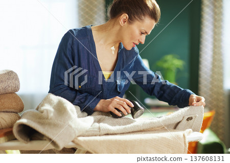 Woman Using Fabric Shaver on Winter Coat at Home 137608131