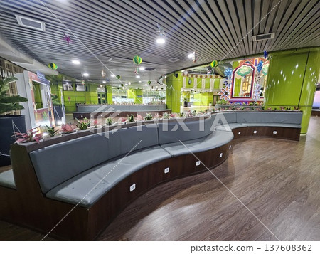 A modern waiting lounge featuring curved grey cushioned benches with integrated power outlets, decorated with festive green hanging ornaments and potted plants under a contemporary slatted ceiling. 137608362