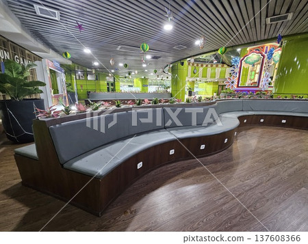A modern waiting lounge featuring curved grey cushioned benches with integrated power outlets, decorated with festive green hanging ornaments and potted plants under a contemporary slatted ceiling. 137608366