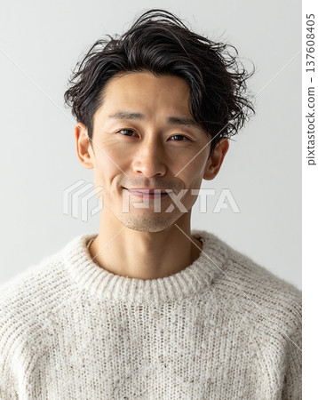 Portrait of a man in his 30s wearing a white knit sweater and smiling gently 137608405