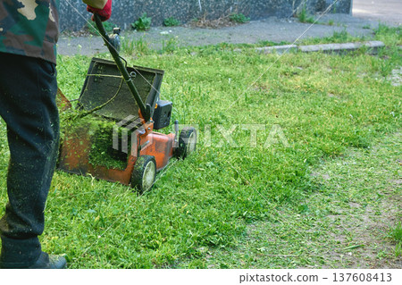 Garden worker with handle lawn mower.Grass cutting on green meadow Garden worker with handle lawn mower.Grass cutting on green meadow 137608413