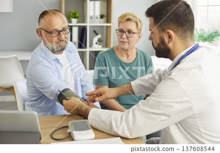 Doctor measuring blood pressure for smiling senior couple during checkup 137608544