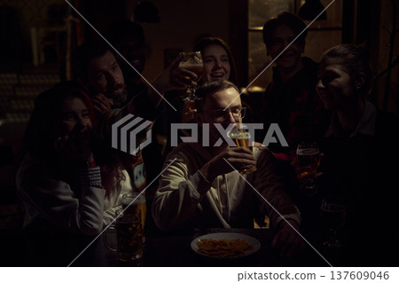 Group of football fans watching game in pub while one man drinks beer calmly during tense match moment 137609046