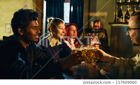 Friends clinking beer glasses in pub during lively social gathering and relaxed nightlife Friends clinking beer glasses in pub during lively social gathering and relaxed nightlife 137609060