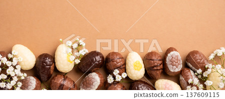 Colorful Easter eggs arranged with delicate white flowers on a brown background for festive decoration Colorful Easter eggs arranged with delicate white flowers on a brown background for festive decoration 137609115
