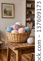 Knitting yarn in various pastel colors arranged in a wicker basket on a wooden table, with a cozy interior and shelves in the background 137609173